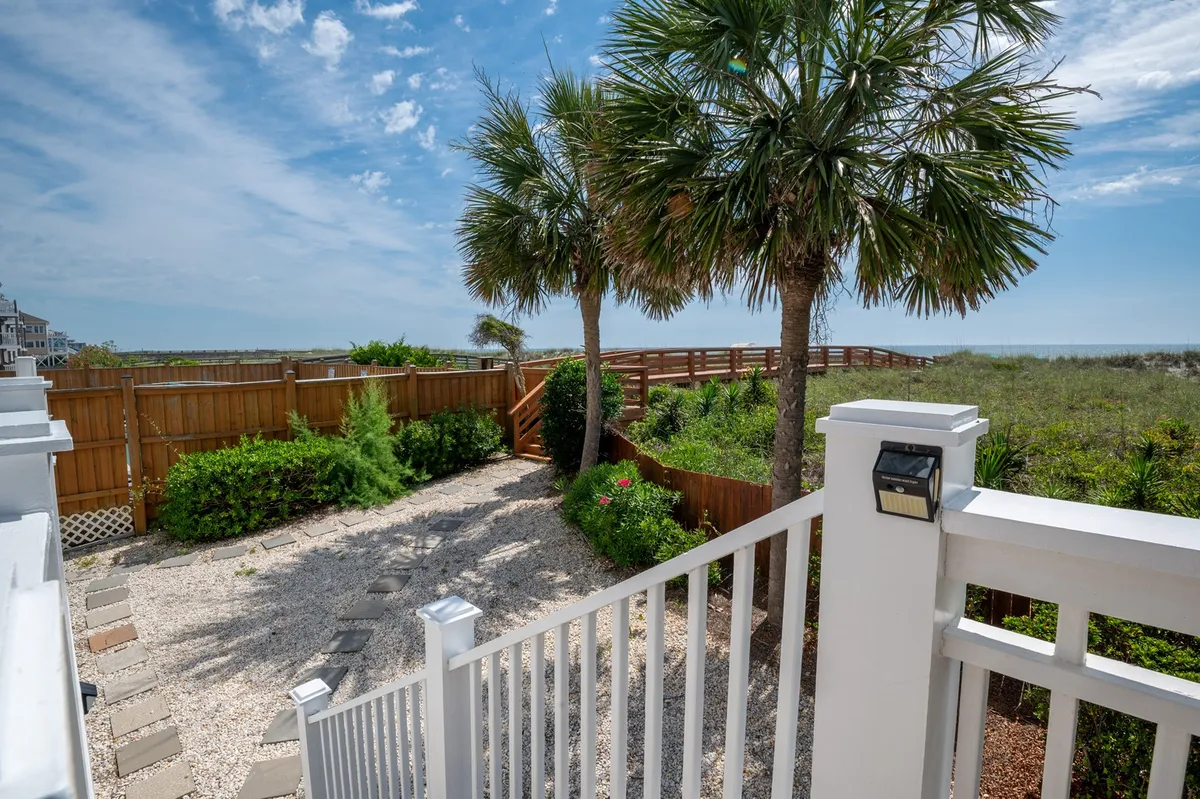 A serene exterior setting with palm trees, a gravel pathway, wooden fence, and a clear beach view. The scene is tranquil and inviting, hinting at outdoor relaxation, intimate celebrations, and stargazing at night.