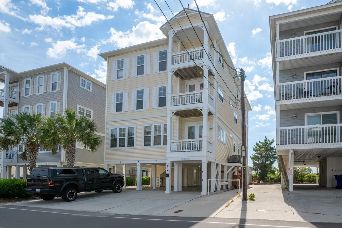 This image showcases the exterior of a tall, multi-level beach house surrounded by palm trees, with parked cars and inviting balconies. The home’s size and design visually suggest its ability to accommodate larger groups or multiple families. The cheerful, welcoming mood sets the stage for collaborative getaways.