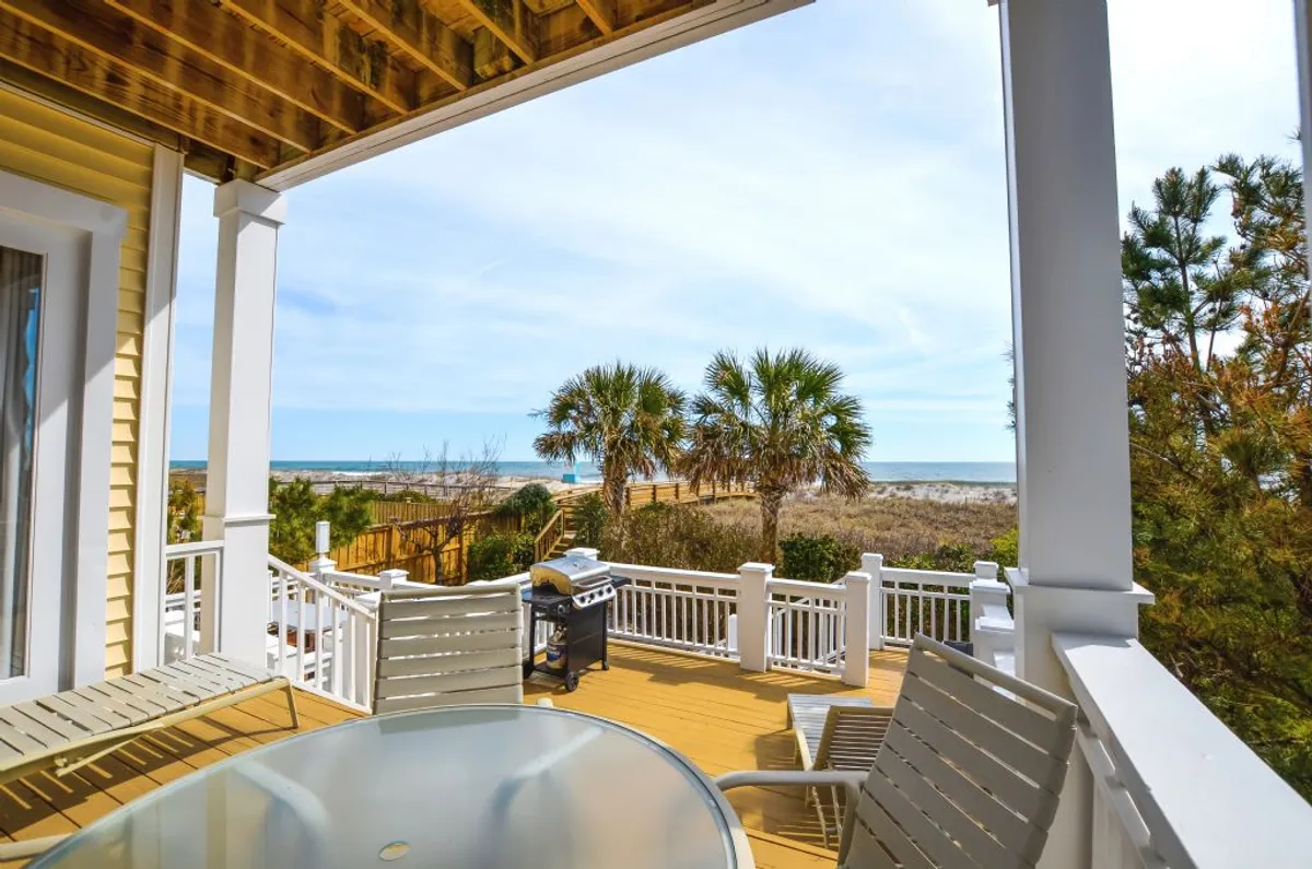 A serene oceanfront deck with comfortable outdoor furniture, palm trees swaying in the background, and an inviting grill. The scene overlooks the ocean, ideal for both sunrise coffee and evening cocktails. The tranquil setting is enhanced by soft lighting and unobstructed water views.