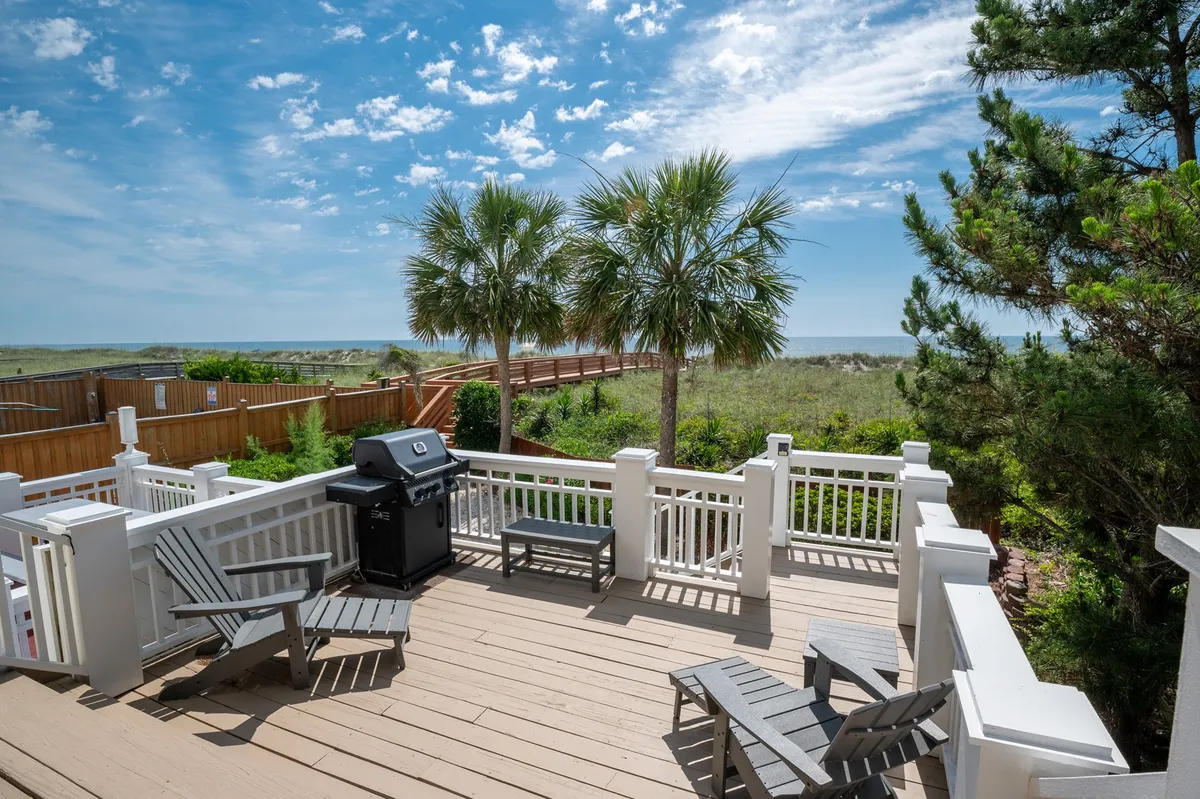 A deck with comfortable seating, a grill, palm trees, and sweeping views of the ocean. The space is clearly set up for group relaxation, cookouts, and sunset gatherings right by the beach, combining indoor-outdoor living.
