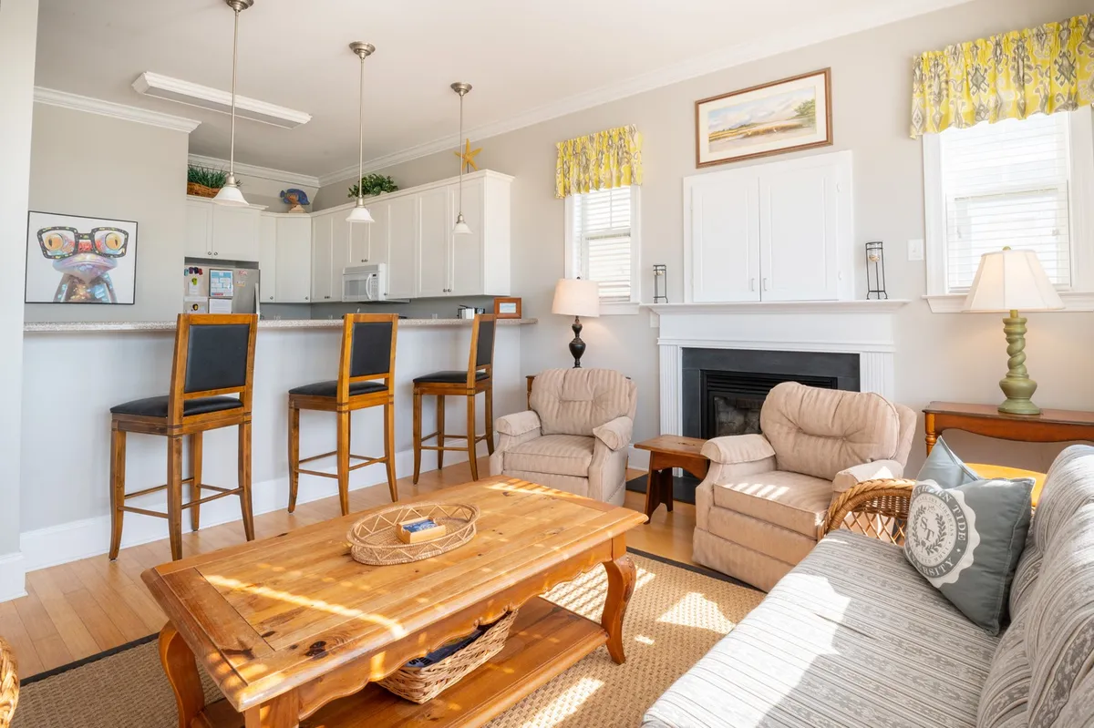A cozy corner of the living space featuring a couch, a wooden coffee table, bar stools at a breakfast counter, and a decorative fireplace. Artwork on the wall adds a homely touch. The fireplace and seating invite guests to unwind together, especially on cozy evenings or during game nights.