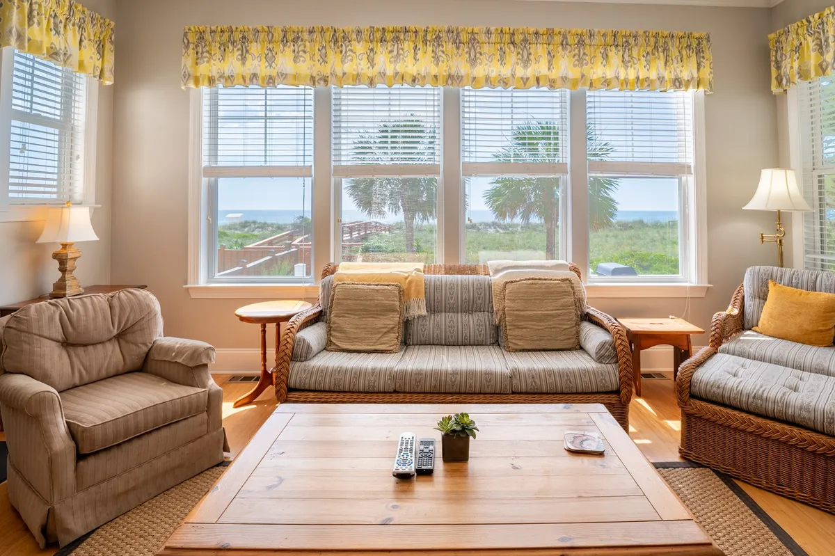 A cozy living space with large windows framing a stunning ocean view, comfortable seating, and a wooden coffee table. The room is filled with natural light, suggesting a welcoming spot for family gatherings, reading, or relaxing while enjoying the changing seasons outside.