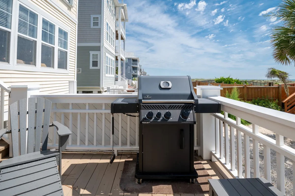 This image features a grill and outdoor seating area overlooking the ocean, with the expansive water view visible in the background. The scene suggests opportunities for outdoor dining and relaxation, framed by natural light and the sounds of the sea.