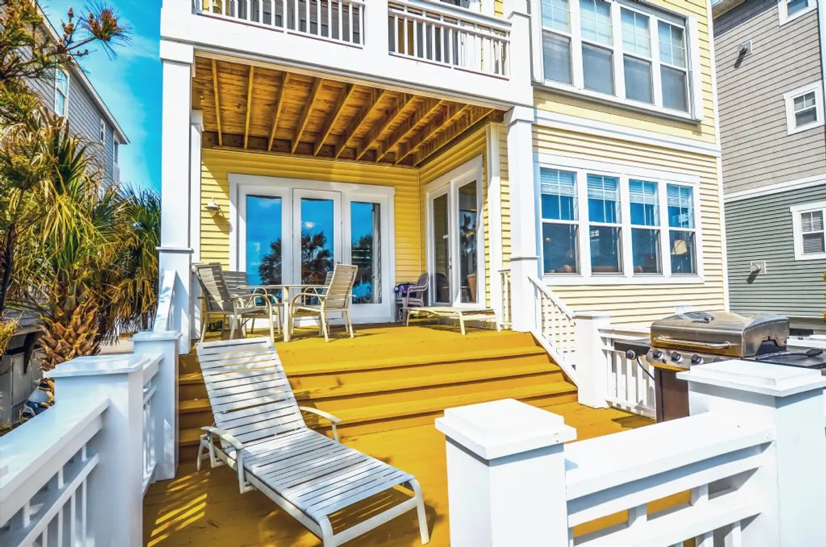 A relaxed outdoor seating area on a deck, featuring a grill and surrounded by palm trees. The inviting setup is ideal for socializing, enjoying the view, and making the most of the coastal location with group barbecues or morning coffee.