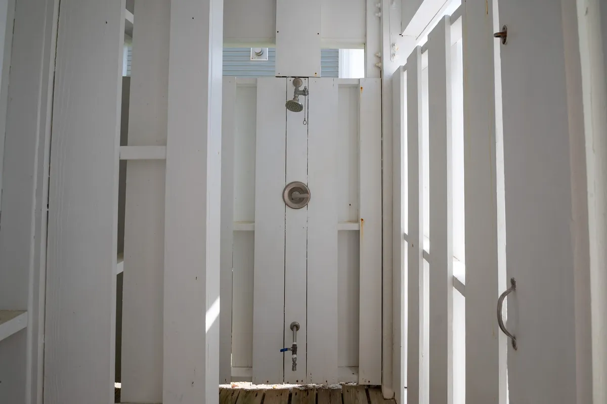 A refreshing outdoor shower with wooden flooring and white wooden panels offers a private yet open-air spot to rinse off after a day on the sand. The space feels serene and thoughtfully designed for post-beach convenience.