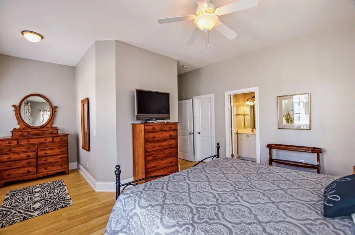 A calm and well-appointed bedroom with a king bed dressed in patterned bedding, a wooden dresser, mirror, television, and a closet door. The ambiance suggests comfort and relaxation, suitable for friends or grandparents.